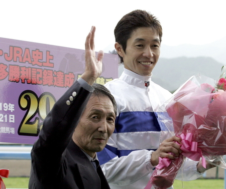 ＪＲＡ最多勝利記録を更新した武豊騎手は父・武邦彦調教師（左）から花束を受け取り笑顔を見せる＝２００７年７月２１日、小倉競馬場